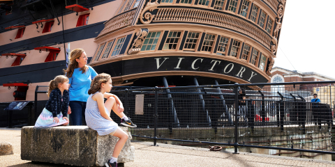 Family sitting in front of HMS Victory at Portsmouth Historic Dockyard