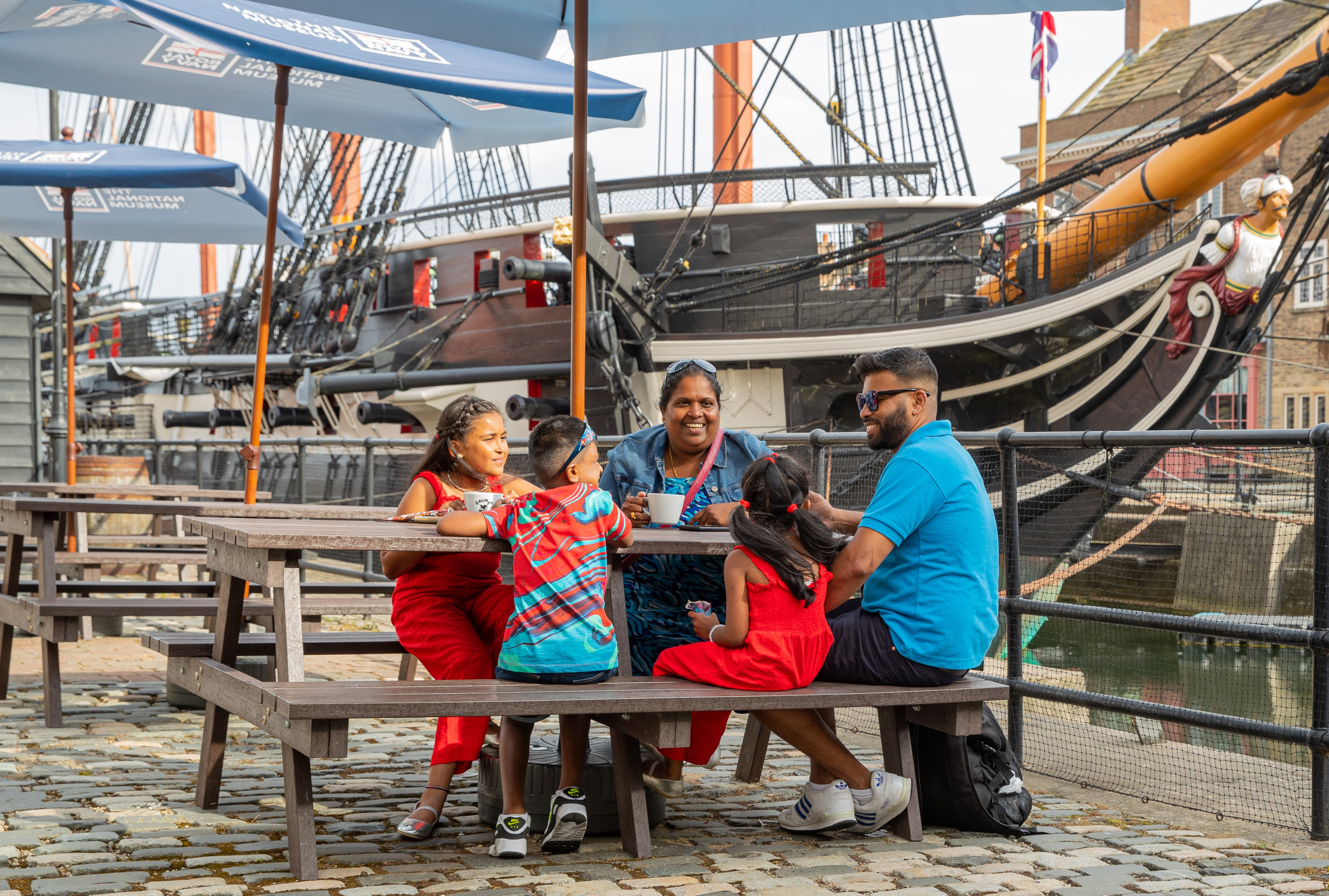 A family sitting on a bench in front of HMS Trincomalee