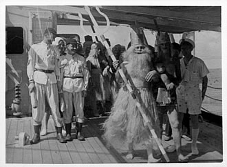 A man dressed as Poseidon is surrounded by naval personnel in fancy dress