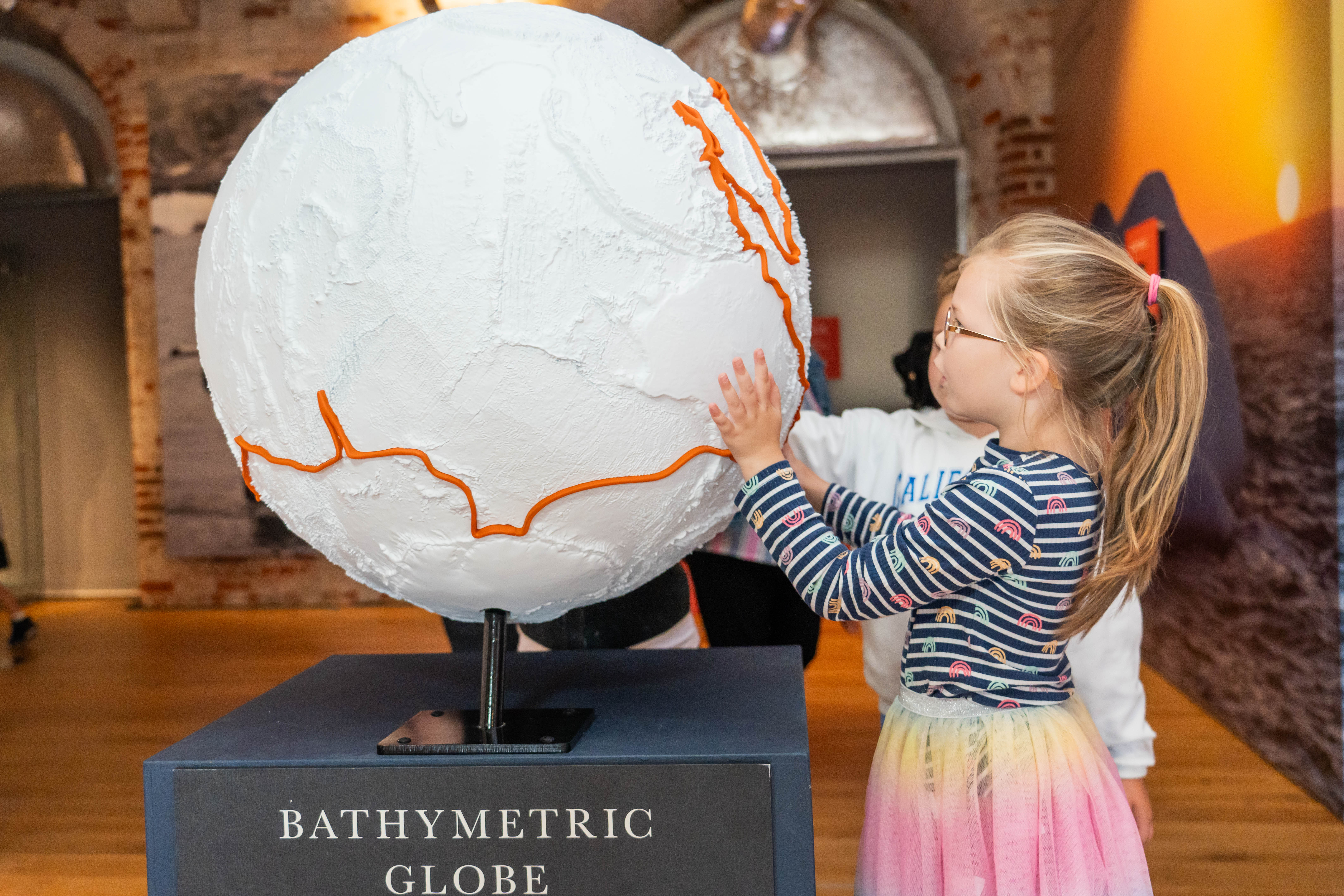Child touches bathymetric globe display at Worlds Beneath the Waves exhibition 