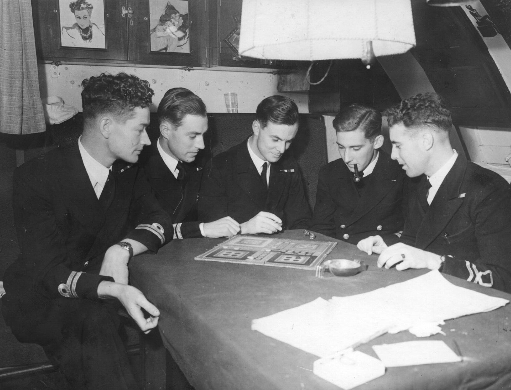Five men gathered around a table on a submarine playing a board game