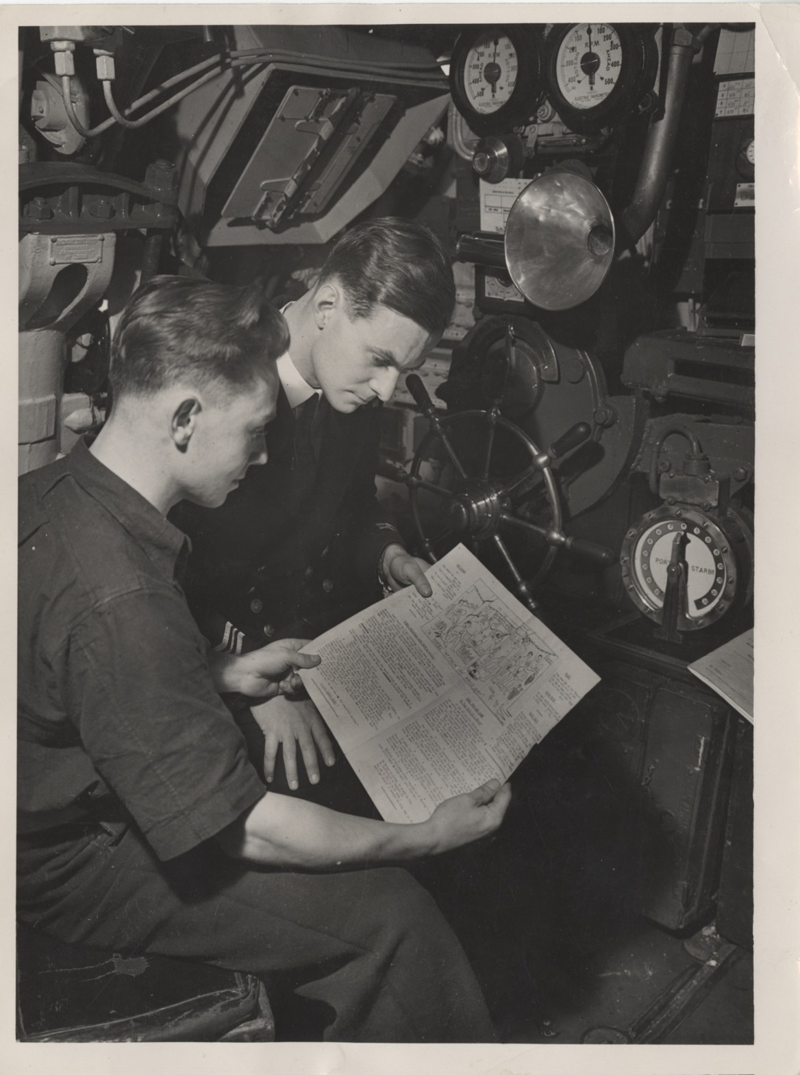 Two men read a newspaper onboard a submarine
