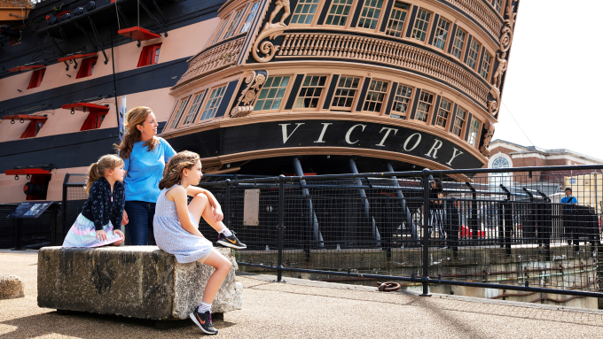 Family sitting in front of HMS Victory at Portsmouth Historic Dockyard