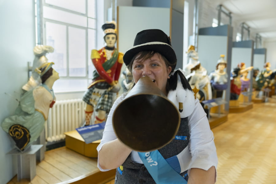 Woman with megaphone in front of navy figureheads