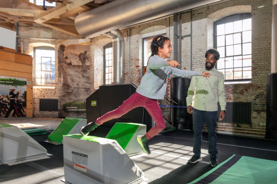 Young girl uses the obstacle course at Action Stations as her father watches. 