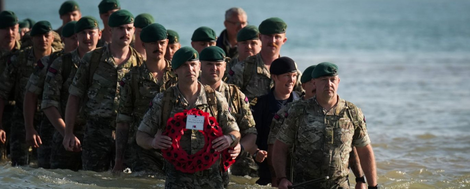Royal Marines with a memorial walking on the beach. 