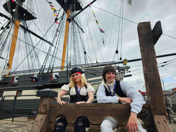 Two costume interpreters sit in the stocks in front of HMS Trincomalee in Hartlepool