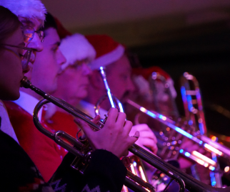 7 brass instrument players playing their instruments, while wearing Christmas hats.