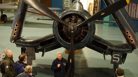 People standing around a propeller aircraft listening to the guide speaking