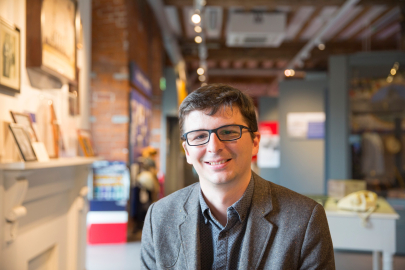 A person smiles facing the camera with a museum gallery in the background.