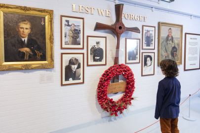 A child looks at a wall with photographs and a poppy-wreath with a sign reading 'lest we forget'