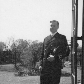 A black and white photo of a man in Royal Navy uniform in front of an open door in a garden