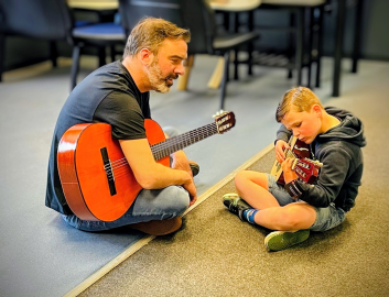 man and boy sitting learning and playing guitars