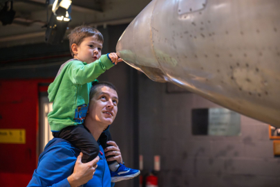 son on fathers shoulders inspecting nose of plane