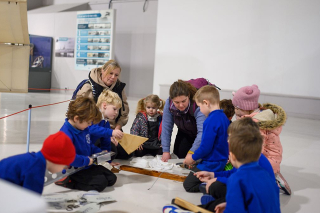 A group of young children play with different textured material in the Fleet Air Arm Musem