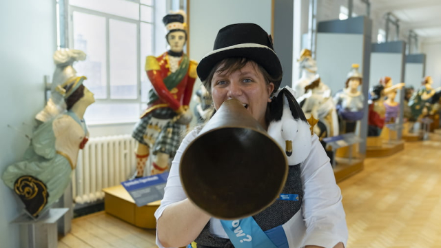 Woman with megaphone in front of navy figureheads