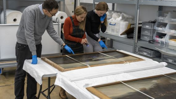 Three curators from the National Museum of the Royal Navy look over some fine art from the collection.