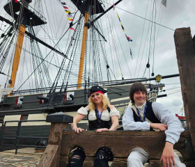 Two costume interpreters sit in the stocks in front of HMS Trincomalee in Hartlepool 