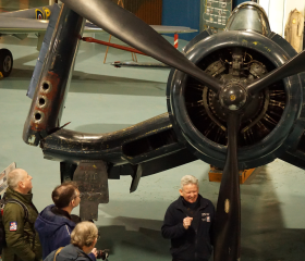 People standing around a propeller aircraft listening to the guide speaking