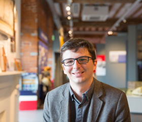 A person smiles facing the camera with a museum gallery in the background.