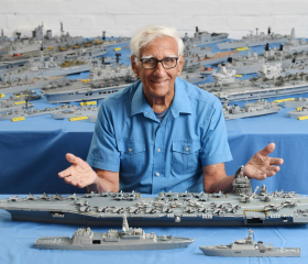 Phillip Warren sat in front of a model carrier made from matchsticks