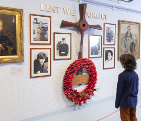 A child looks at a wall with photographs and a poppy-wreath with a sign reading 'lest we forget'