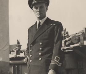A black and white photo of a man in Royal Navy uniform next to machinery