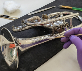 A gloved hand cleans a trombone with a tiny brush. 