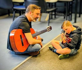 A man and boy sitting on the floor and playing guitars.