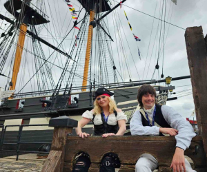 Two costume interpreters sit in the stocks in front of HMS Trincomalee in Hartlepool 