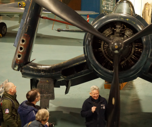 People standing around a propeller aircraft listening to the guide speaking