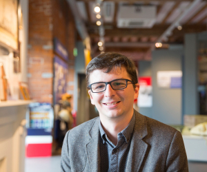A person smiles facing the camera with a museum gallery in the background.
