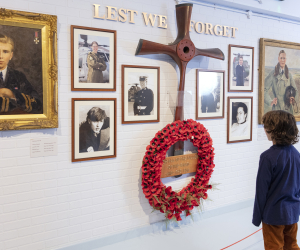 A child looks at a wall with photographs and a poppy-wreath with a sign reading 'lest we forget'
