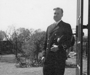 A black and white photo of a man in Royal Navy uniform in front of an open door in a garden