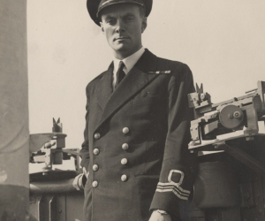 A black and white photo of a man in Royal Navy uniform next to machinery
