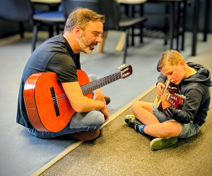 man and boy sitting learning and playing guitars