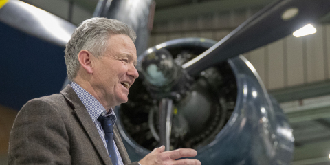 Man speaking in front of blue plane