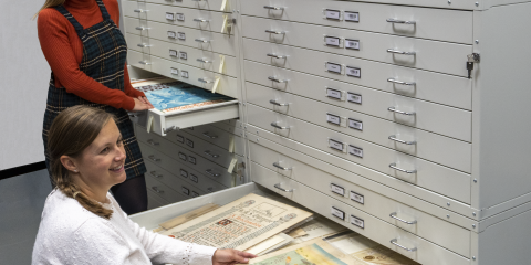 Two women next to open drawers full of documents