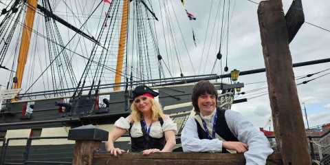Two costume interpreters sit in the stocks in front of HMS Trincomalee in Hartlepool 