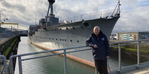 John Taylor, who served onboard HMS Caroline as an engineer, pictured infront of the ship